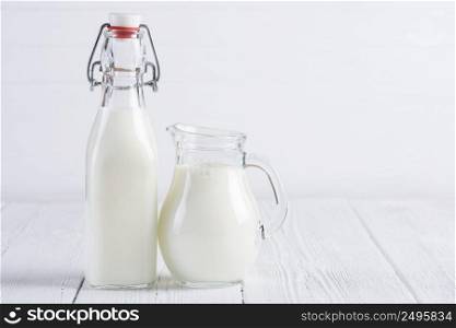 Jar with milk and vintage bottle of milk on white wooden table background still life