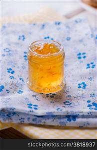 Jar with orange jam over blue napkin, selective focus