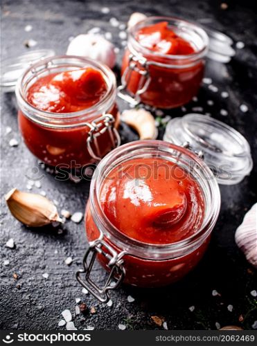 Jars of tomato sauce with garlic and salt. On a black background. High quality photo. Jars of tomato sauce with garlic and salt.