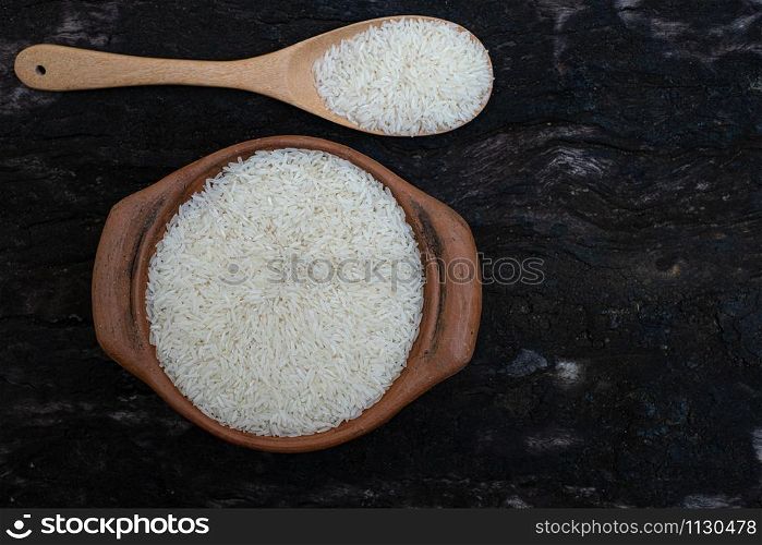 Jasmine rice in a clay pot and the wood ladle isolated on wood background