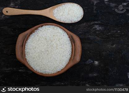 Jasmine rice in a clay pot and the wood ladle isolated on wood background