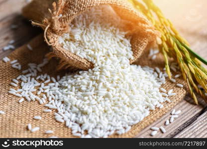 Jasmine white rice in sack and harvested yellow rip rice paddy on wooden table, harvest rice and food grains cooking concept