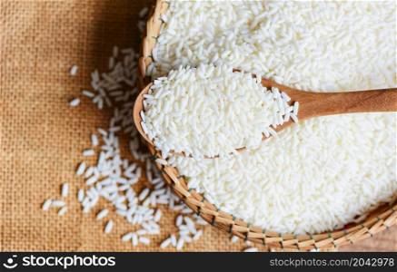 Jasmine white rice on wooden spoon on the basket in the the sack, harvest rice and food grains cooking concept