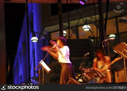 Jazz singer on outdoor stage clapping hands, blurred by long exposure