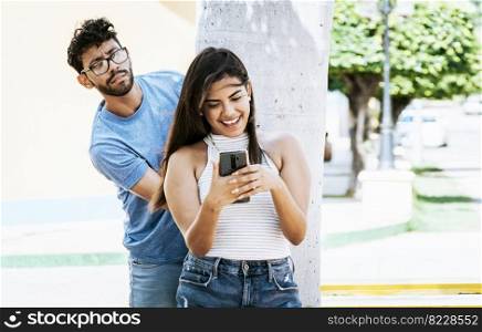 Jealous boyfriend spying on his girlfriend’s cell phone in the park, Jealous man spying on his girlfriend texting on the cell phone. Suspicious man spying on his girlfriend with his cell phone