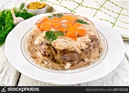Jellied pork and beef with carrots and parsley on a plate, towel, garlic and dill on the background light wooden boards