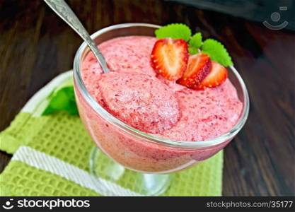 Jelly air strawberry in a glass bowl with a spoon, mint on a green towel on a background of wooden boards