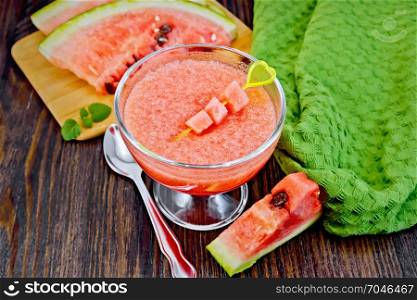 Jelly airy watermelon in a glass bowl, spoon, towel on a background of a dark wooden board