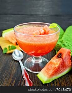 Jelly airy watermelon in a glass bowl, spoon, towel on a wooden plank background