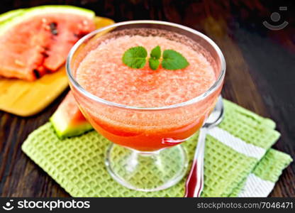 Jelly airy watermelon with mint in a glass bowl, spoon on a green towel on a wooden plank background