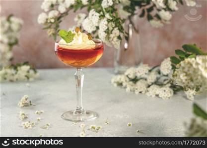 Jelly dessert. Delicious fruit dessert with curd cream in elegant stemware glass on gray table surface surround of spirea white blossom.