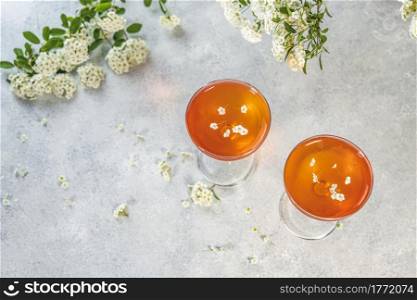 Jelly dessert. Two elegant stemware glass of delicious fruit dessert in on gray table surface surround of spirea white blossom.