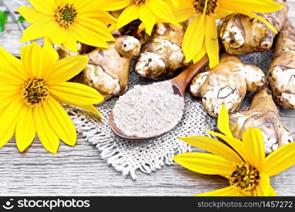 Jerusalem artichoke flour in a spoon on a burlap with flowers and vegetables on background of an old wooden board