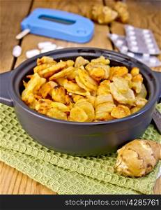 Jerusalem artichokes roasted in a roasting pan, fresh tubers of Jerusalem artichoke on a napkin, the meter and pills on the background of wooden boards