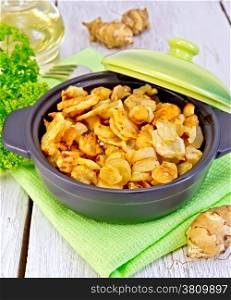 Jerusalem artichokes roasted in a roasting pan with a lid, fresh tubers of on a napkin, parsley, vegetable oil on a background of white wooden plank