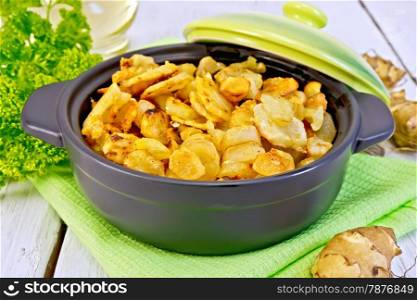 Jerusalem artichokes roasted in roasting pan with lid, fresh tubers on a napkin, parsley, vegetable oil on background of white wooden plank