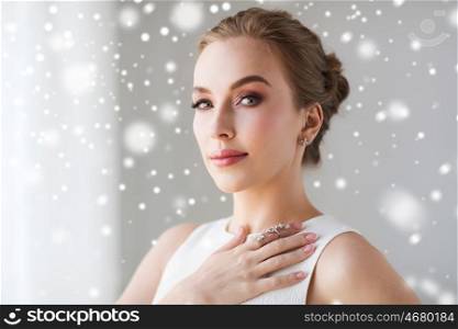 jewelry, luxury, christmas, holidays and people concept - beautiful woman in white dress with diamond earring and ring over snow. beautiful woman in white with diamond jewelry