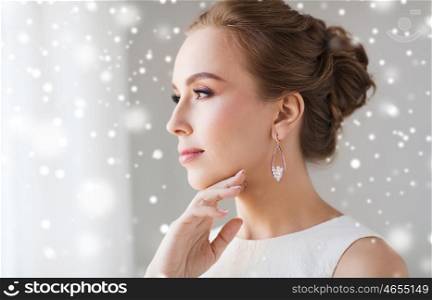 jewelry, luxury, christmas, holidays and people concept - close up of beautiful woman in white dress wearing pearl earring over snow