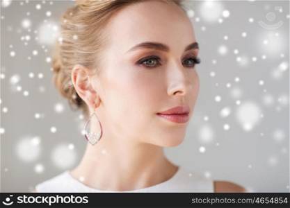 jewelry, luxury, christmas, holidays and people concept - close up of woman in white wearing pearl earring over gray background and snow
