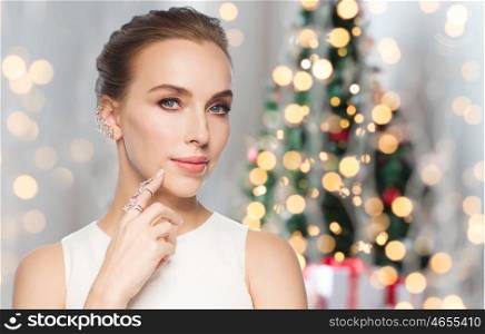jewelry, luxury, christmas, holidays and people concept - smiling woman in white dress with diamond earring and ring over lights background