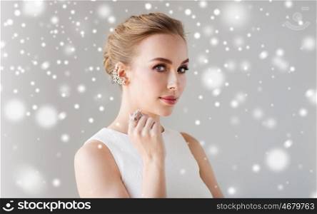 jewelry, luxury, christmas, holidays and people concept - smiling woman in white dress with diamond earring and ring over gray background and snow