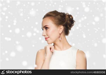 jewelry, luxury, christmas, holidays and people concept - smiling woman in white dress wearing pearl earrings over gray background and snow