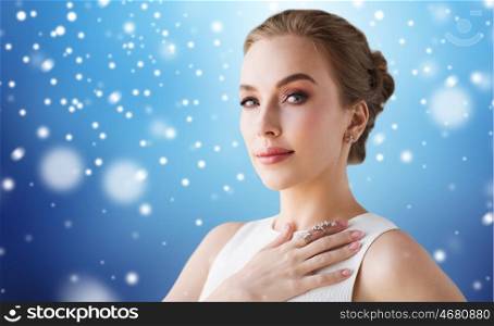 jewelry, luxury, christmas, holidays and people concept - smiling woman in white dress with diamond earring and ring over blue background and snow