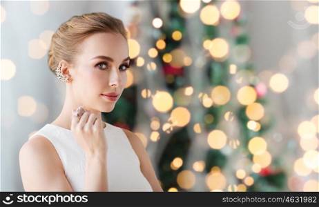 jewelry, luxury, holidays and people concept - smiling woman in white dress with diamond earring and ring over christmas tree lights background
