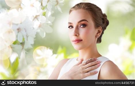 jewelry, luxury, wedding and people concept - smiling woman in white dress with diamond earring and ring over natural spring cherry blossom background