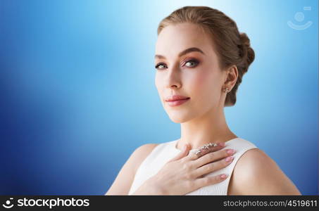 jewelry, luxury, wedding and people concept - smiling woman in white dress with diamond earring and ring over blue background