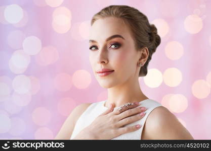 jewelry, luxury, wedding and people concept - smiling woman in white dress with diamond earring and ring over rose quartz and serenity lights background
