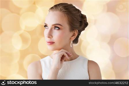 jewelry, luxury, wedding and people concept - smiling woman in white dress with diamond earring over holidays lights background