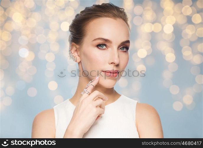 jewelry, luxury, wedding and people concept - smiling woman in white dress with diamond earring and ring over holidays lights background