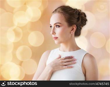 jewelry, luxury, wedding and people concept - smiling woman in white dress with diamond earring and ring over beige holidays lights background