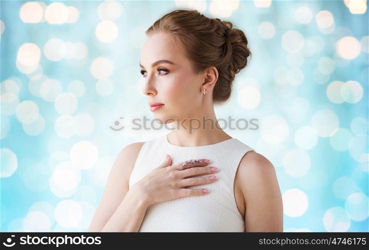 jewelry, luxury, wedding and people concept - smiling woman in white dress with diamond earring and ring over blue holidays lights background