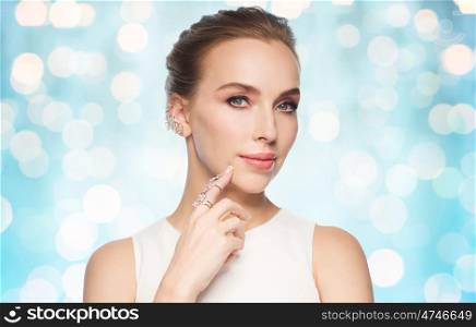 jewelry, luxury, wedding and people concept - smiling woman in white dress with diamond earring and ring over blue holidays lights background