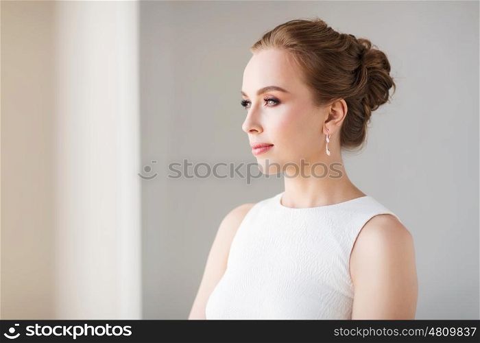 jewelry, luxury, wedding and people concept - smiling woman in white dress with diamond earring