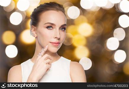 jewelry, luxury, wedding, holidays and people concept - beautiful woman in white dress with diamond ring and earring over lights background