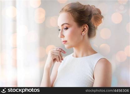 jewelry, luxury, wedding, holidays and people concept - smiling woman in white dress with diamond earring and ring over lights effect