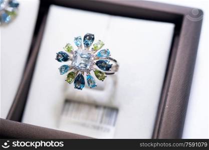jewelry retail store showcase displaying white gold ring with precious gemstones. ring with huge sapphires, topazes diamonds, emeralds. close up