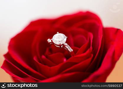 jewelry, romance, proposal, valentines day and holidays concept - close up of diamond engagement ring in red rose flower