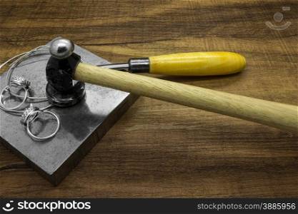 Jewelry tools and classic silver rings on a wooden background.