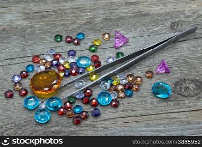 Jewelry tweezers and multicolored gems on a wooden background.