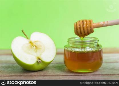 Jewish holiday, Apple Rosh Hashanah dessert, on the photo have honey in jar and green apples was sliced on wooden with green background