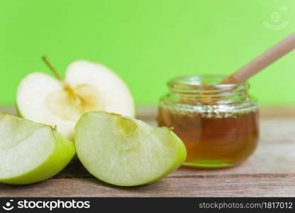 Jewish holiday, Apple Rosh Hashanah, on the photo have honey in jar and drop honey on green apples on wooden with green background