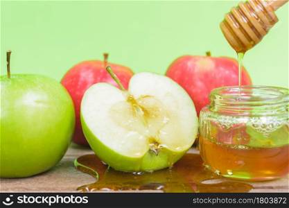 Jewish holiday, Apple Rosh Hashanah, the photo have honey in jar and drop honey on green apples on wooden with green background