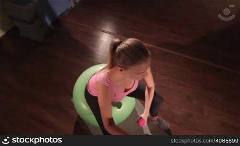 JIB CRANE: Fit woman exercising on fitness ball with light weight dumbbells in gym high-angle view