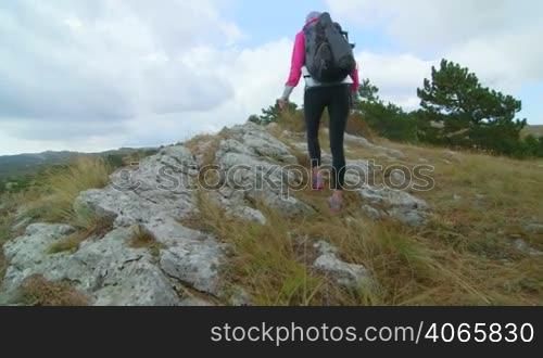 JIB CRANE: Woman day hiking in Crimean mountains walking along edge of cliff rear view