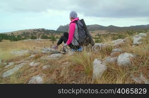 JIB CRANE: Woman hiker with backpack relaxing on top of mountain plateau looking at highlands, rear view