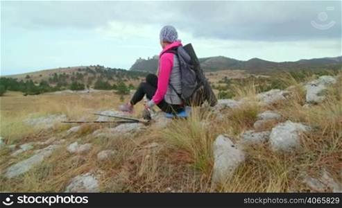 JIB CRANE: Woman hiker with backpack relaxing on top of mountain plateau looking at highlands, rear view